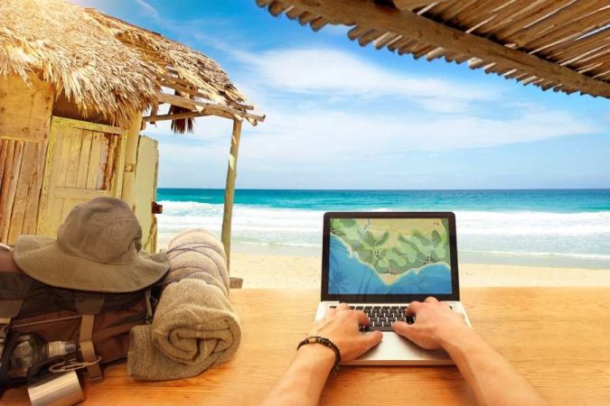 Digital nomad working on laptop at tropical beach location while managing digital nomad taxes remotely