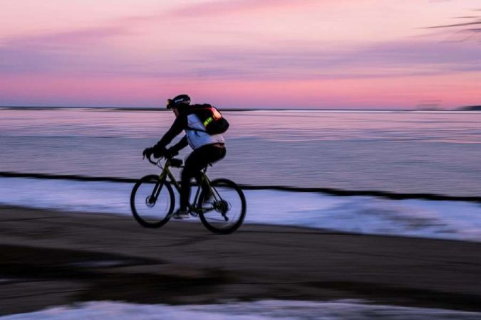 A beginner cyclist ride along a coastal path at sunset, with a pink and purple sky reflecting over calm water.