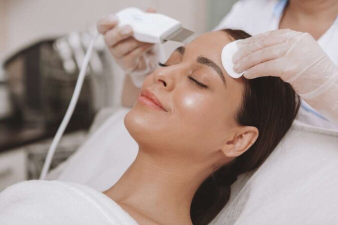 A professional aesthetician performing a spa facial treatment with a skin-cleansing device.