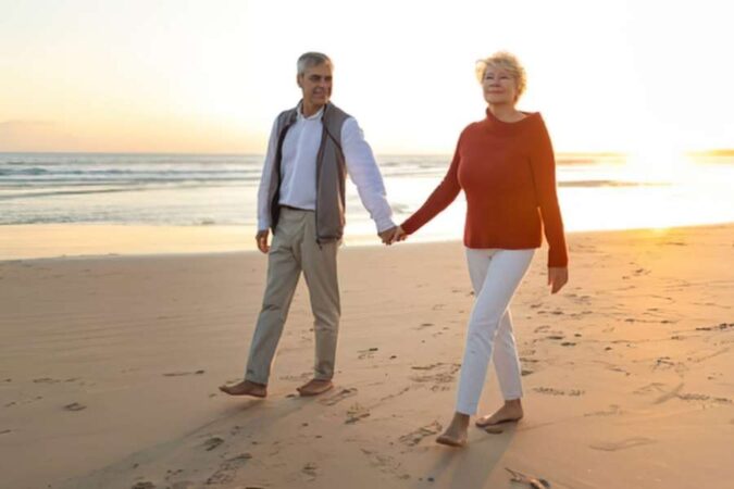 An older couple enjoying a peaceful sunrise walk along the sandy beach.