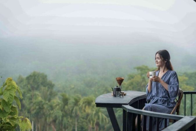 A woman enjoying her morning with a cup of coffee on a scenic balcony during a Floating Lake Stay.